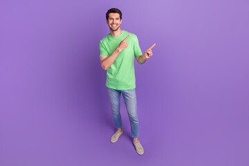 Fototapeta na wymiar Full length size photo of young guy wear green stylish t-shirt jeans direct fingers empty space ad isolated on violet color background