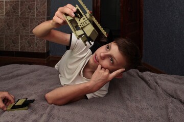 in the evening, the boy is engrossed in the game, playing and assembling a constructor on a mat on...