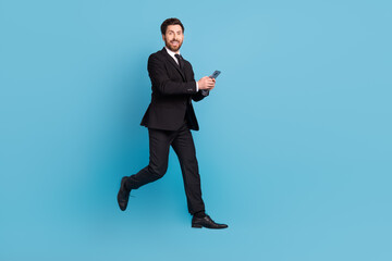 Fototapeta na wymiar Full length photo of confident funny recruiter wear black tuxedo jumping texting modern device empty space isolated blue color background