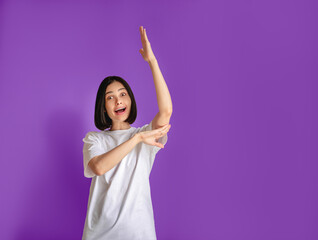 The student girl raised her hand to ask a question. Active female student on a purple background. A cadet in a white T-shirt. Caucasian student with short hair and dark hair.