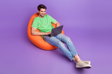 Full body cadre of user technologies man working special office zone lying pouf dormitory with netbook isolated on violet color background