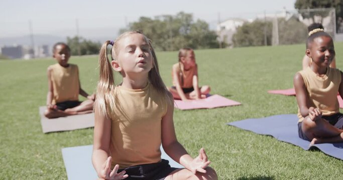 Focused diverse schoolgirls practicing yoga and meditating at stadium in slow motion