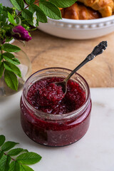 Glass jar with homemade edible rose jam on marble-wooden board.