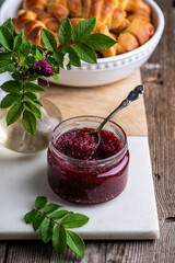 Glass jar with homemade edible rose jam on marble-wooden board.