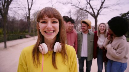 Young girl laughing funny looking at camera outdoors with group of friends. Happy people having fun together focus on pretty young girl. College buddies on campus. Leisure in the park in autumn.