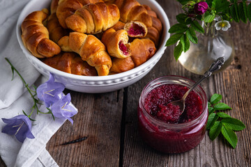 Glass jar with homemade edible rose jam and crescents with rose jam on old wooden table.