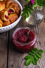 Glass jar with homemade edible rose jam and crescents with rose jam on old wooden table.