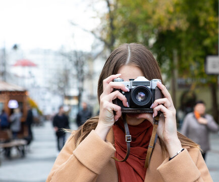 Girl on the street looks through the lens of a vintage camera
