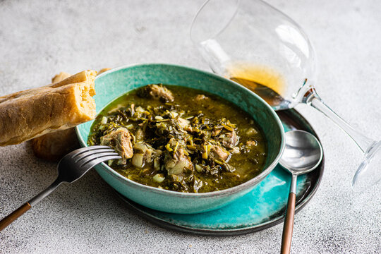 Close-up of a bowl of traditional Georgian lamb and green plum stew (Chakapuli) with fresh bread and a glass of wine
