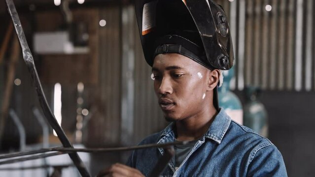 Young black male working on steel structure with welding gear in workshop slow motion