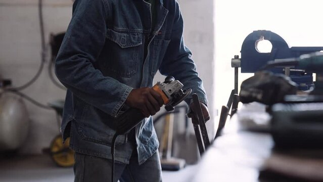 Young black male with denim jacket using angle grinder power tool in workshop with sparks