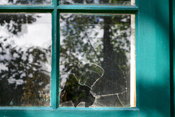 A clear transparent pane of glass in a green wood antique window broken with a hole from a gunshot....