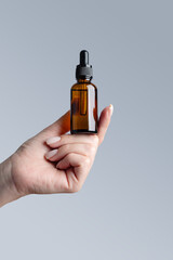 Beautiful groomed woman's hand with amber glass serum bottle mock up on a gray background.