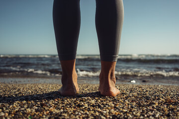 close-up of female feet barefoot standing on the sand against the background of the sea