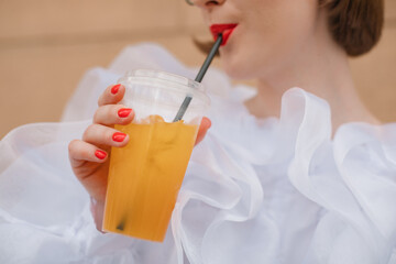 Glamorous woman in a ruffled blouse standing outdoors drinking a fruit drink