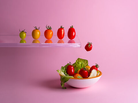 Row of assorted multi coloured tomatoes jumping off a diving board into a bowl of salad