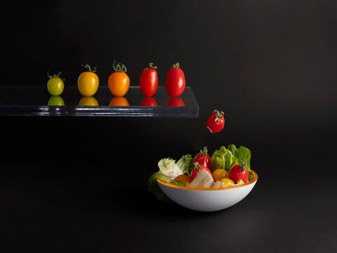 Row of assorted multi coloured tomatoes jumping off a diving board into a bowl of salad