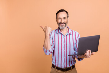 Portrait of handsome cheerful corporate man hold netbook direct finger empty space offer ad isolated on beige color background