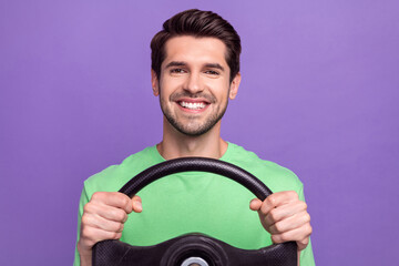 Portrait of satisfied cheerful guy with bristle wear green t-shirt holding steering wheel driving car isolated on violet color background
