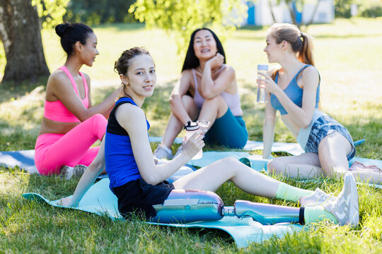 Young beautiful woman with leg bionic prosthesis after workout with a group of college girl friends. Concept of support of disabled people, university community, diversity and inclusion in daily life