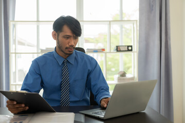 Fototapeta premium Young african man working with analytics sitting in beautiful workplace with laptop computer and financial report analysis concept document. monthly account
