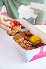 Red velvet brioche mini doughnut lifted by a hand from a box of assorted donuts.