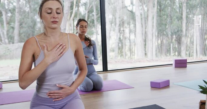 Diverse women with hands on chest and stomach practicing breathing exercise on mats