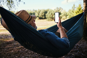 Adult man laying in hammock using mobile phone during summer vacation