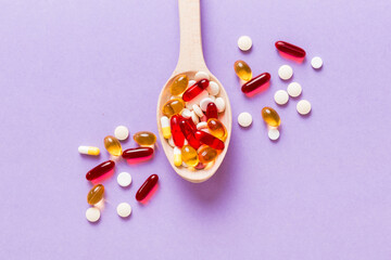 Vitamin capsules in a spoon on a colored background. Pills served as a healthy meal. Red soft gel...