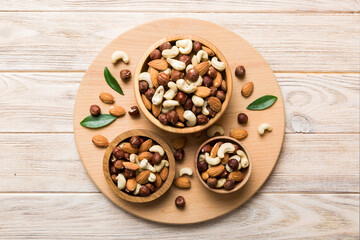Fototapeta premium Assortment of nuts in wooden bowl on colored table. Cashew, hazelnuts, walnuts, almonds. Mix of nuts Top view with copy space