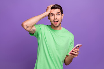 Portrait of astonished impressed guy with bristle wear green t-shirt hold smartphone arm on head...