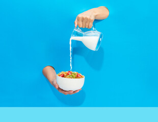a hand pours milk from a jug into a bowl