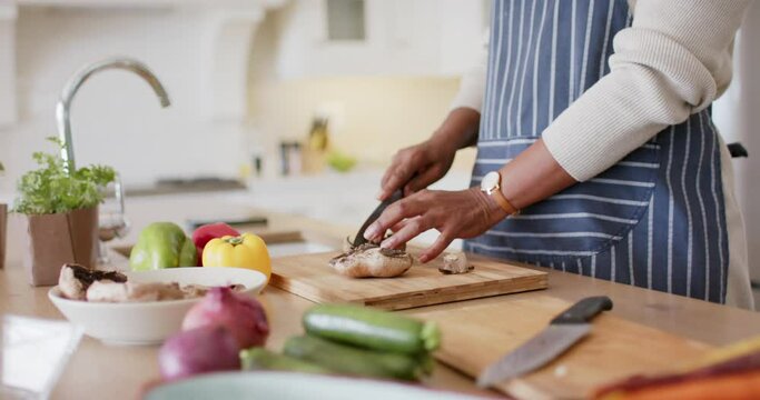 Happy african american senior woman in apron chopping vegetables in kitchen, slow motion