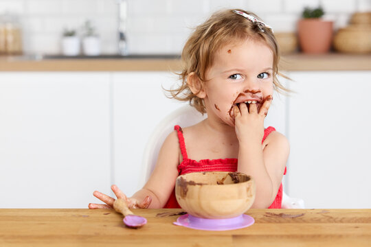 Funny baby girl eating chocolate mousse with fingers
