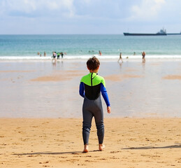 A boy in a neoprene wet suit heads out to sea on a beach