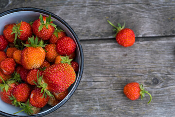 a cup with red strawberries, scattered berries on a wooden background