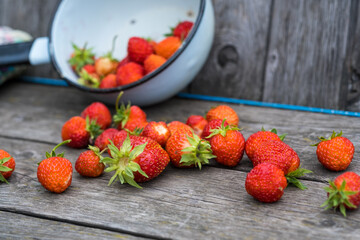 a cup with red strawberries, scattered berries on a wooden background