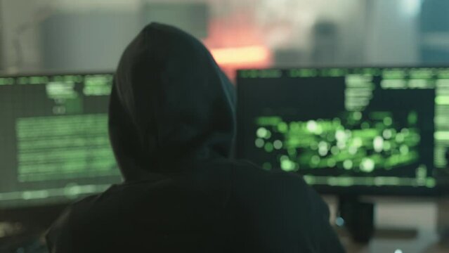 Mysterious cyber security hacker in hoodie in headquarter with computers
