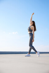 Fototapeta na wymiar Full-length image of young athletic woman taking care of her body, training outdoors on warm sunny day. Stretching