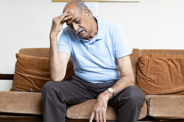 Tired, depressed senior man sitting on couch in living room feeling hurt and lonely. Aged,...
