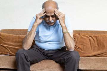 Tired, depressed senior man sitting on couch in living room feeling hurt and lonely. Aged,...