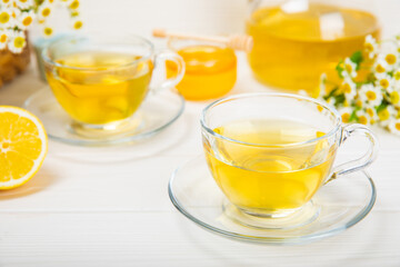 Chamomile herbal tea with flower buds, honey and lemon on a white wooden table and a bouquet of chamomile. Useful herbal, soothing drinks and natural healer concept. Immunity tea.Close up. Copy space.