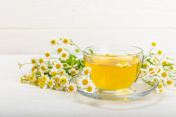 Chamomile herbal tea with flower buds, honey and lemon on a white wooden table and a bouquet of chamomile. Useful herbal, soothing drinks and natural healer concept. Immunity tea.Close up. Copy space.