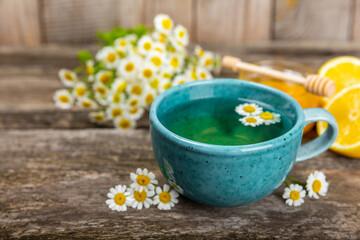Chamomile herbal tea with flower buds, honey and lemon on a brown wooden table and a bouquet of chamomile. Useful herbal, soothing drinks and natural healer concept. Immunity tea.Close up. Copy space.