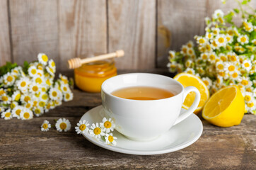 Chamomile herbal tea with flower buds, honey and lemon on a brown wooden table and a bouquet of chamomile. Useful herbal, soothing drinks and natural healer concept. Immunity tea.Close up. Copy space.