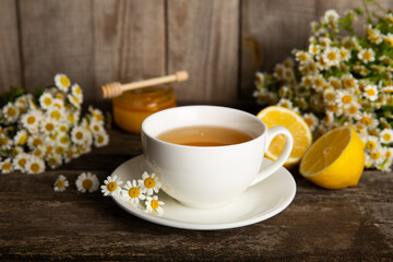 Chamomile herbal tea with flower buds, honey and lemon on a brown wooden table and a bouquet of chamomile. Useful herbal, soothing drinks and natural healer concept. Immunity tea.Close up. Copy space.