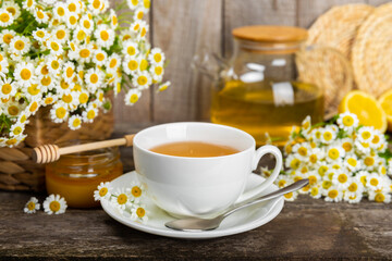 Obraz na płótnie Canvas Chamomile herbal tea with flower buds, honey and lemon on a brown wooden table and a bouquet of chamomile. Useful herbal, soothing drinks and natural healer concept. Immunity tea.Close up. Copy space.