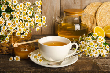 Chamomile herbal tea with flower buds, honey and lemon on a brown wooden table and a bouquet of chamomile. Useful herbal, soothing drinks and natural healer concept. Immunity tea.Close up. Copy space.
