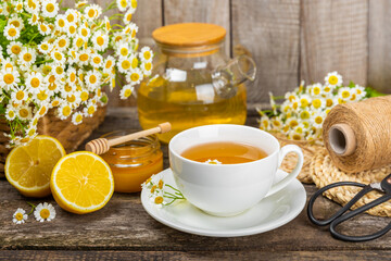 Chamomile herbal tea with flower buds, honey and lemon on a brown wooden table and a bouquet of chamomile. Useful herbal, soothing drinks and natural healer concept. Immunity tea.Close up. Copy space.