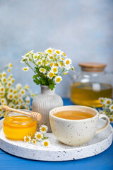 Chamomile herbal tea with flower buds on a blue wooden table and a bouquet of chamomile. Useful herbal, soothing drinks and natural healer concept. Immunity tea.Close up. Copy space.